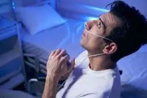 A male patient with a nasal cannula prays in a hospital room