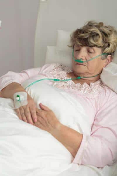 A patient lays in a hospital bed. A nasal cannula helps her receive oxygen from a machine